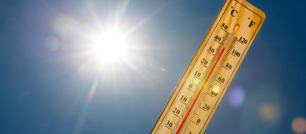 Wooden thermometer showing high temperatures against a bright blue sky with intense sunlight